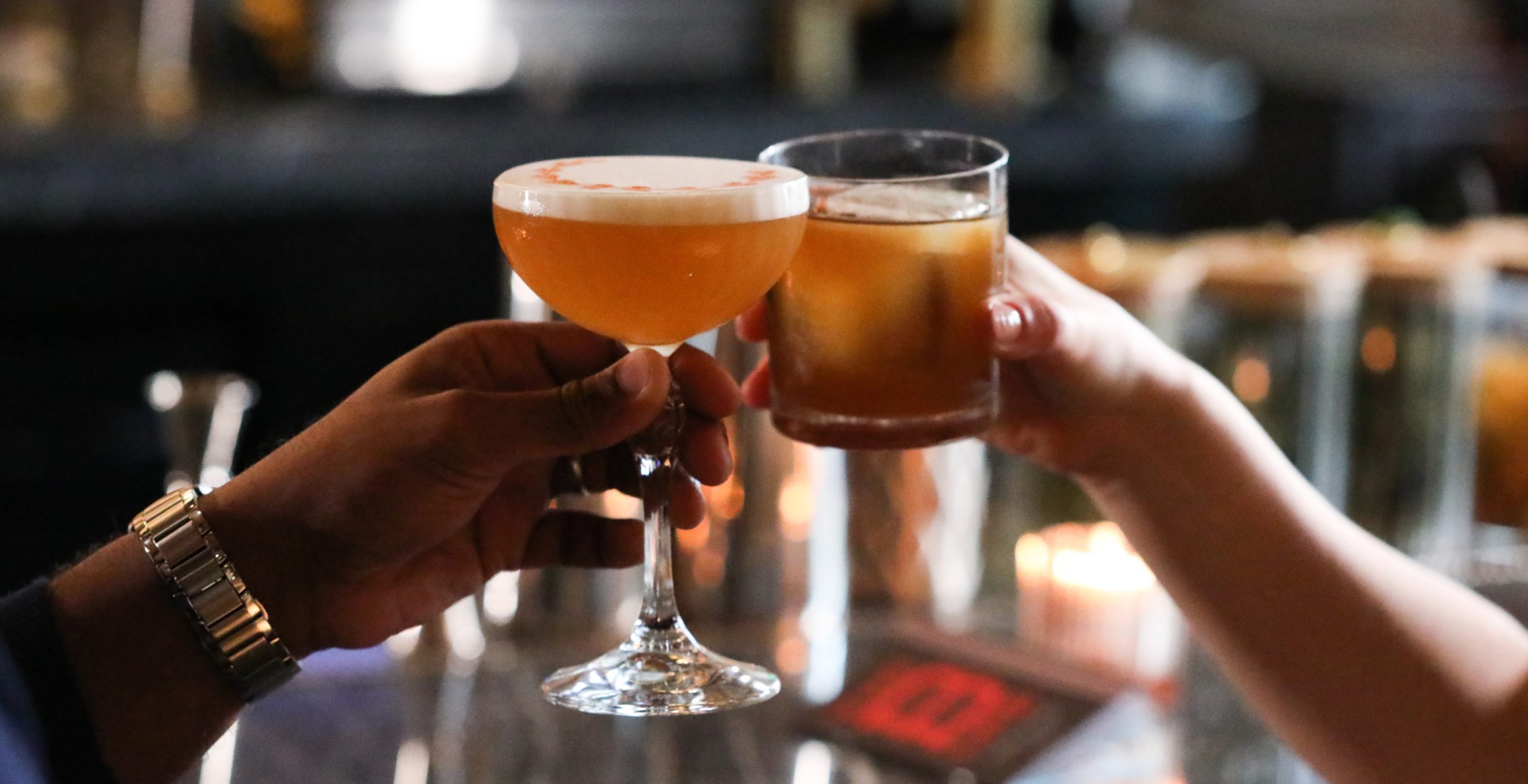 Two people clinking Bourbon drinks.